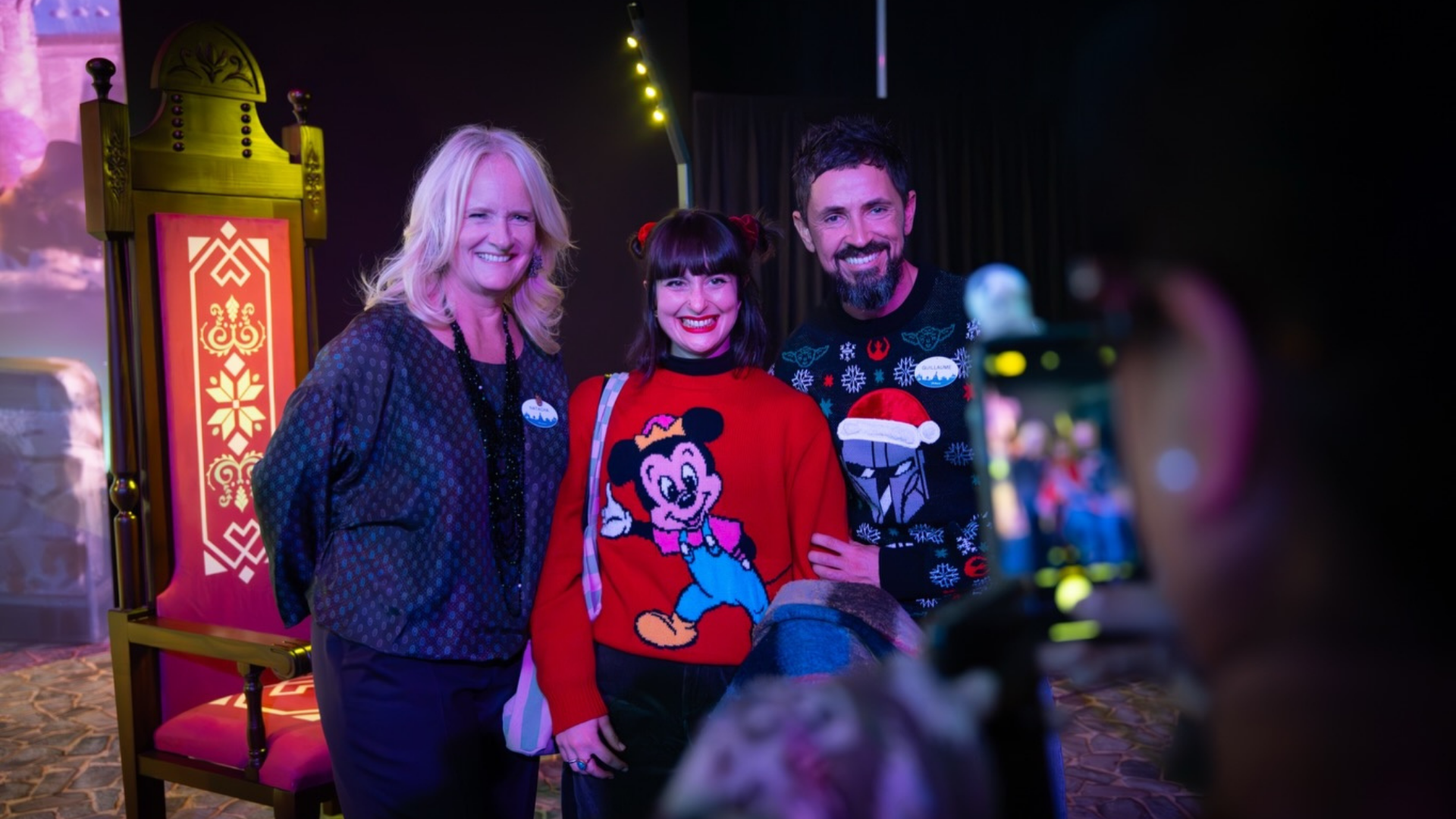 Three people, one wearing a Mickey Mouse sweater, smile for a photo