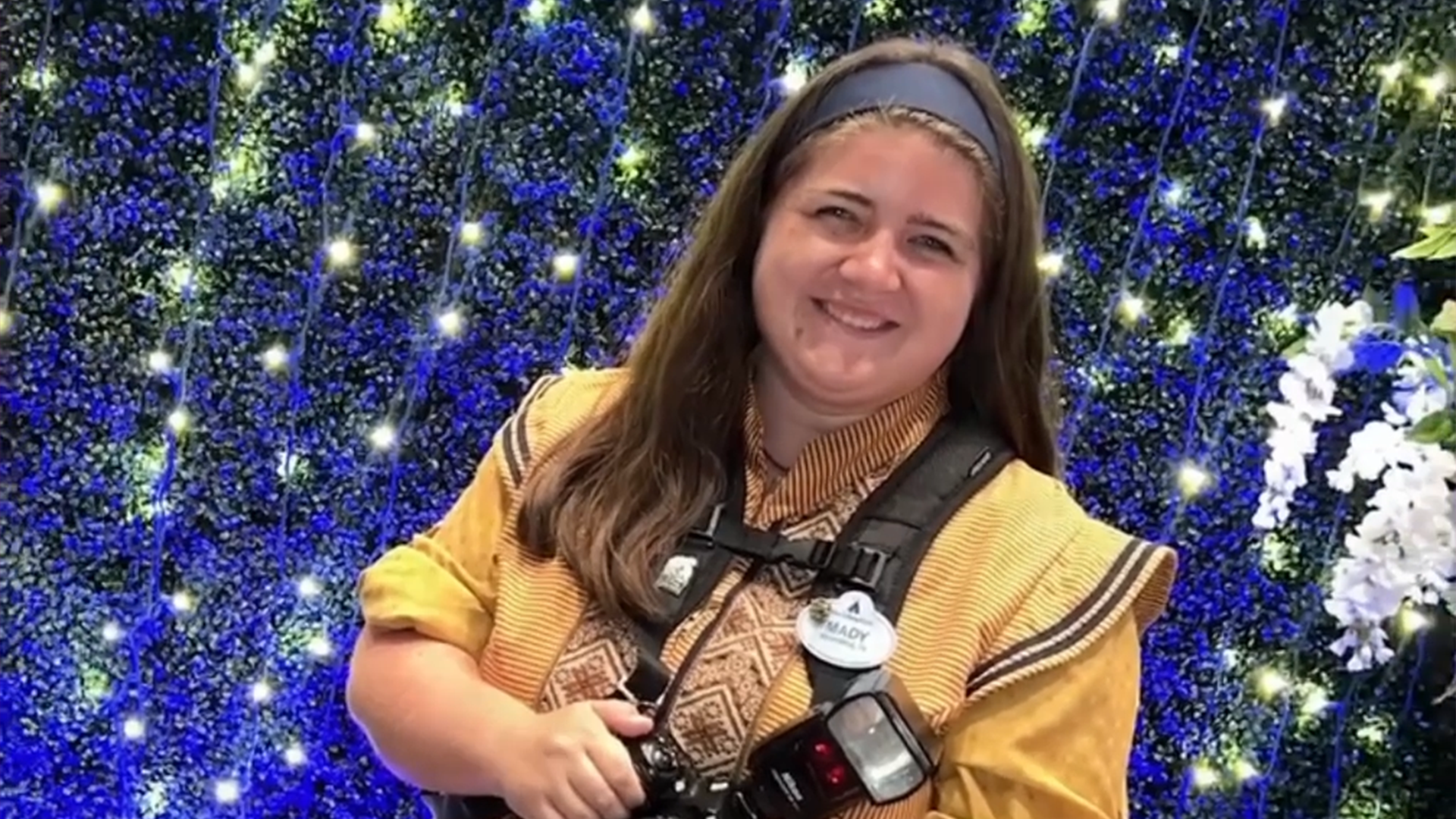 Mady, a Photopass photographer, smiles and holds a camera
