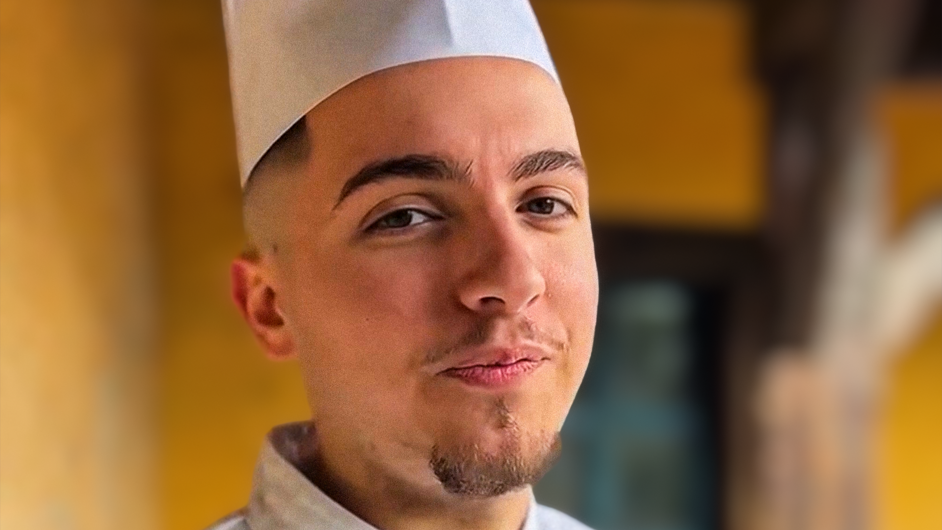 A man in a chef's hat looks at the camera