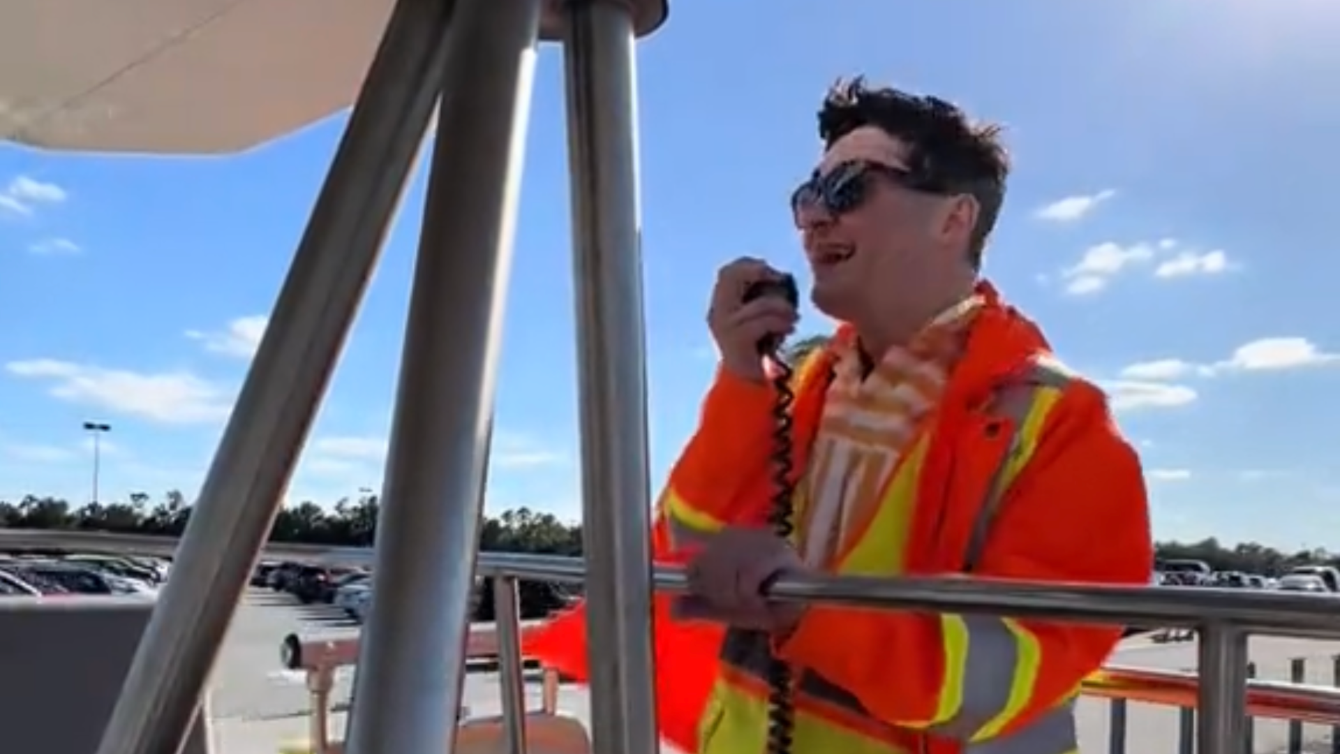 A Disney cast member wears a reflective vest and sunglasses and speaks into a loudspeaker