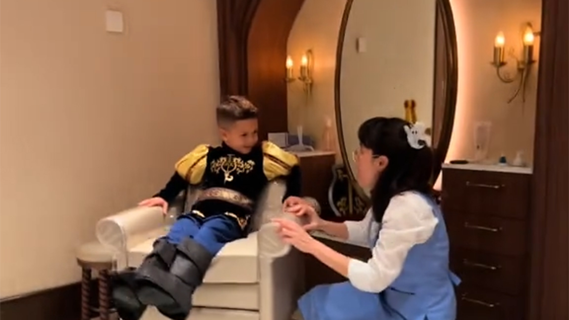 A young boy dressed as a prince sits in a chair and speaks with a woman