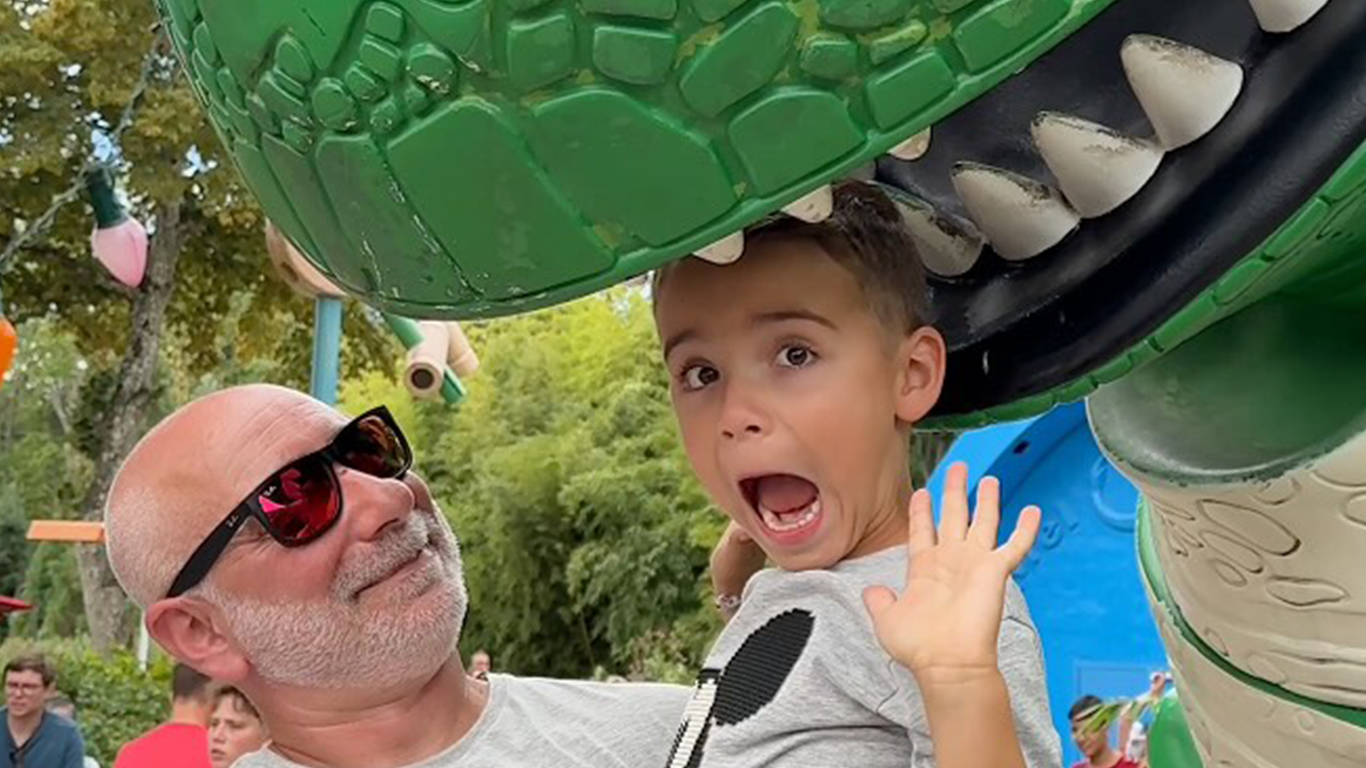 A child is held by a man as a dinosaur appears to bite his head.
