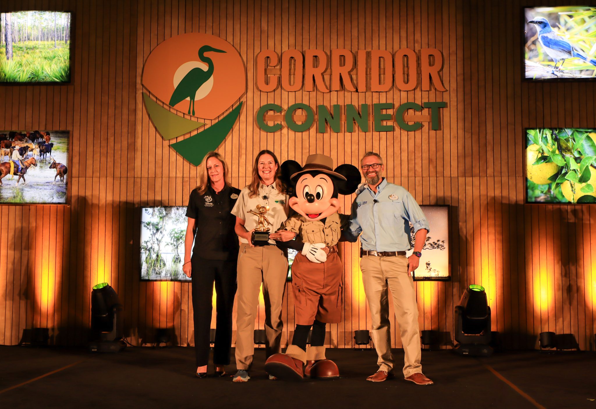 Three people on stage with Mickey Mouse