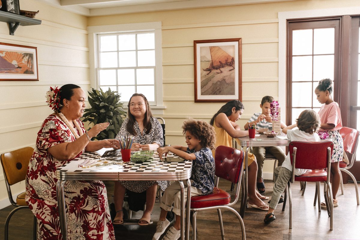 Auntie sitting talking with two tables of children.