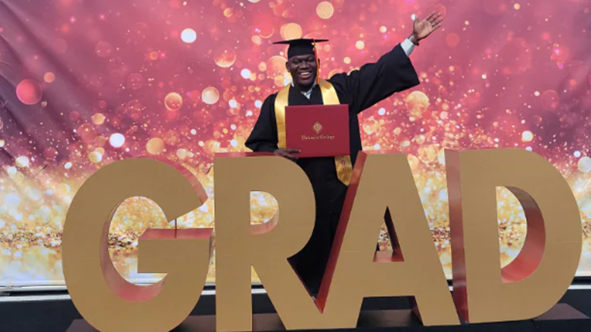 Patrickson in a black cap and gown, holding his diploma, in front of big letters spelling out GRAD.
