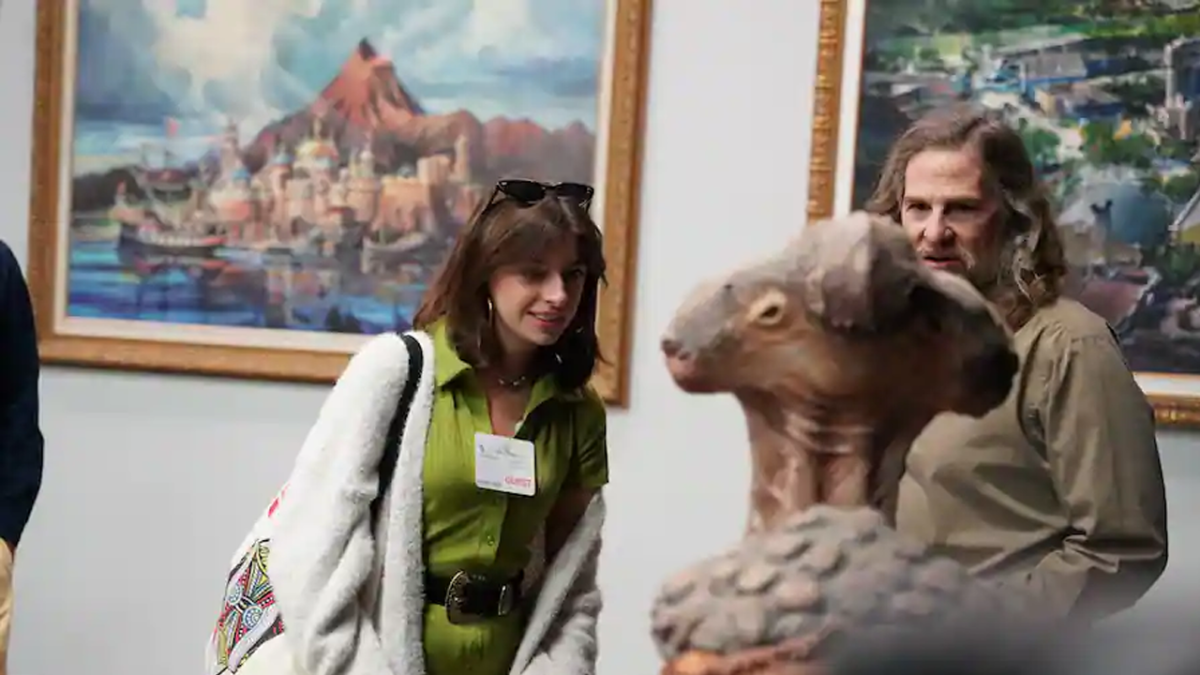 A girl stands with an Imagineer in from of an Audio Animatronic creature.
