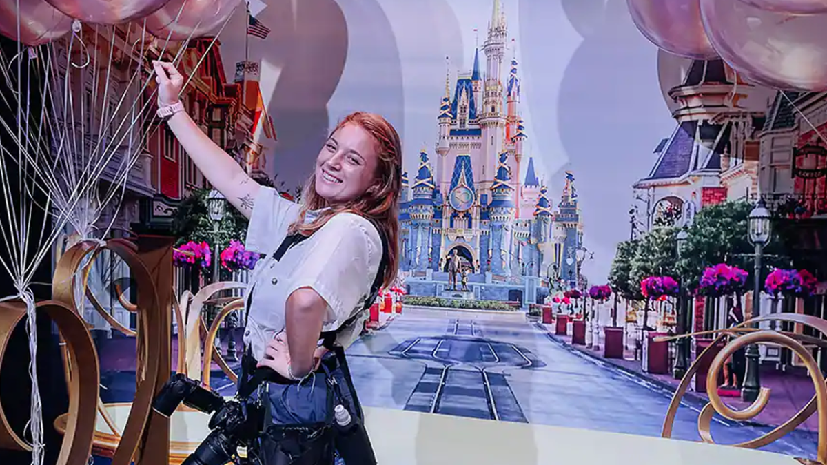 Female Photopass Cast Member posting with a Cinderella Castle backdrop and balloons.