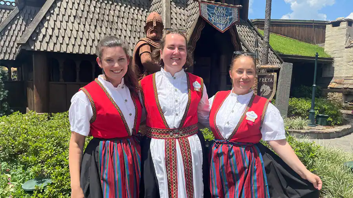 Three female cultural representatives from Norway pose for a picture together in front of the Norway Pavilion.