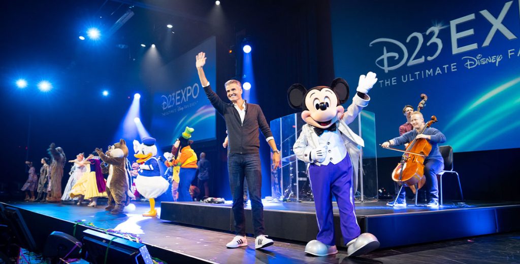 Disney Parks Chairman Josh D'Amaro on stage wit hMickey Mouse at D23 Expo.