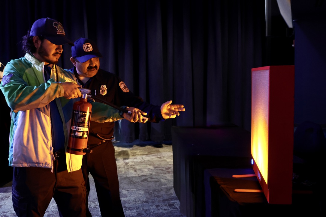 Firefighter Jesse Velarde teaching Disney PhotoPass cast member Juan Carlos Estuvier how to extinguish a fire using the PASS method on the BullEx Bullseye Digital Fire Extinguisher Training System.